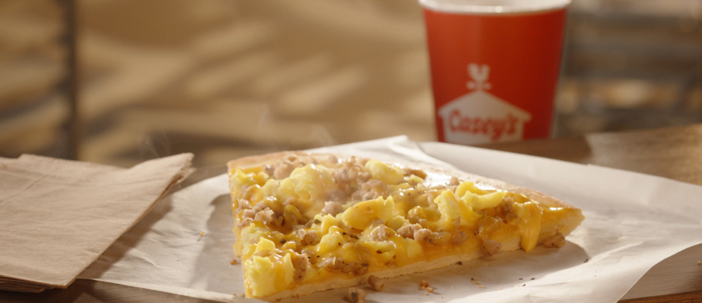 A piece of Casey's breakfast pizza and steaming Casey's coffee