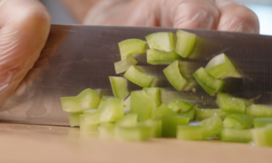 Someone using a knife to cut fresh green peppers