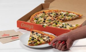 A slice of Casey's Supreme Pizza on a plate in front of the rest of the pie in a box